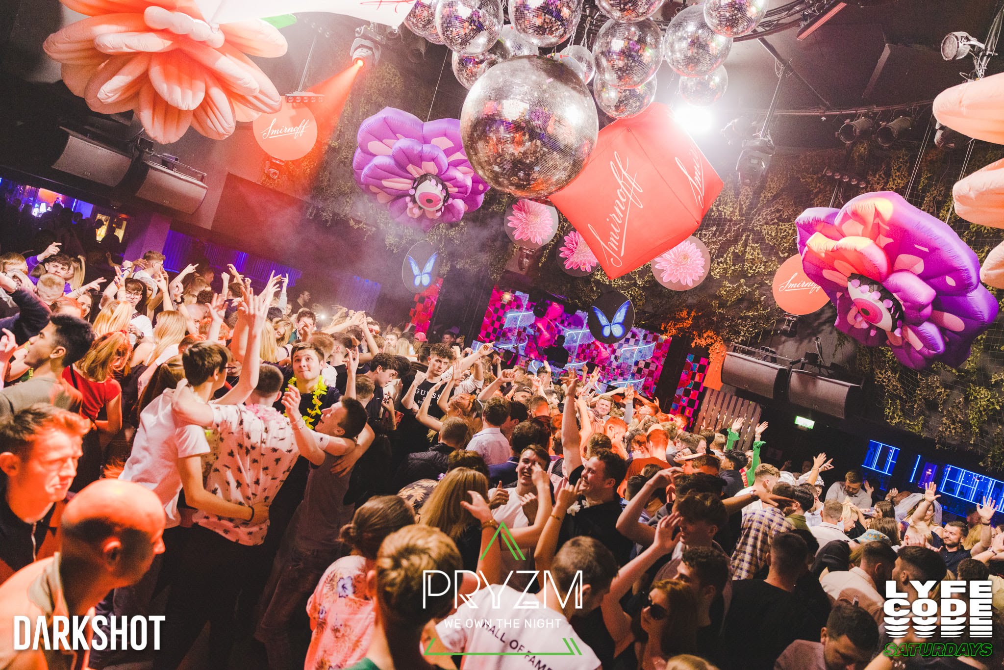 Crowded venue transformed by overhead scenic pieces, mirrored spheres, and colour